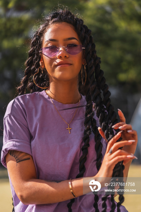 Young smiling dark-skinned woman in purple shirt holding long braids