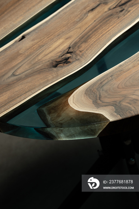 Expensive vintage furniture. The table is covered with epoxy resin and varnished. Luxury quality wood processing. Wooden table on a dark background. A blue epoxy river in a round tree slab.