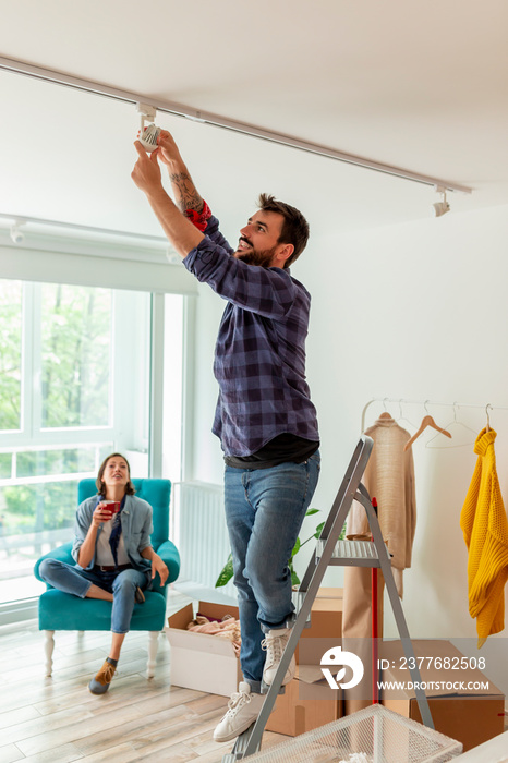 Man changing light bulb while woman is drinking coffee