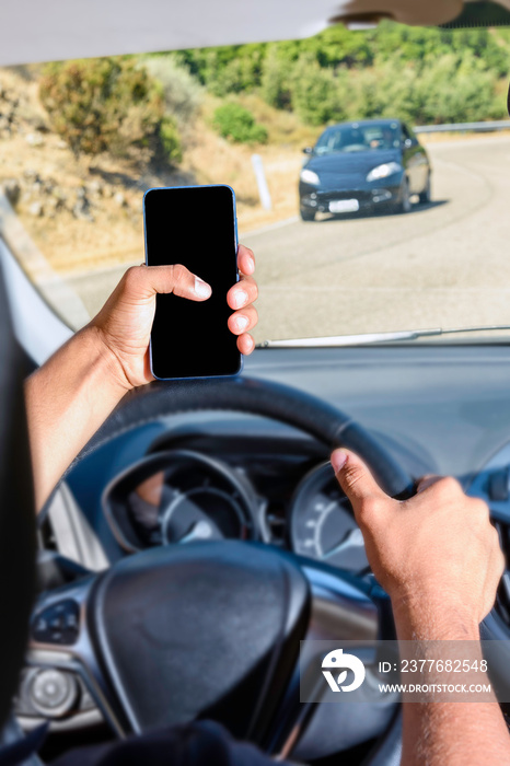 Young driver, using smartphone, on the road in the car.