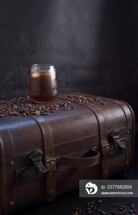 Vaso de café frío con hielo y granos de café en una vieja maleta marrón sobre fondo oscuro