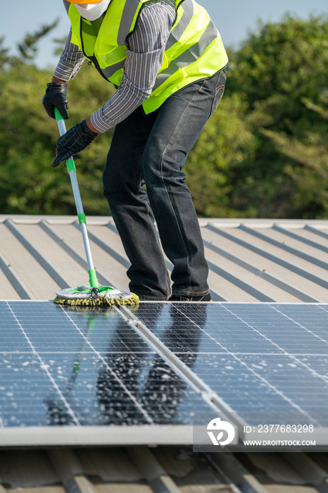 Maintenance technician using cleaning mop and to clean the solar panels that are dirty with dust to improve the efficiency of solar energy storage.