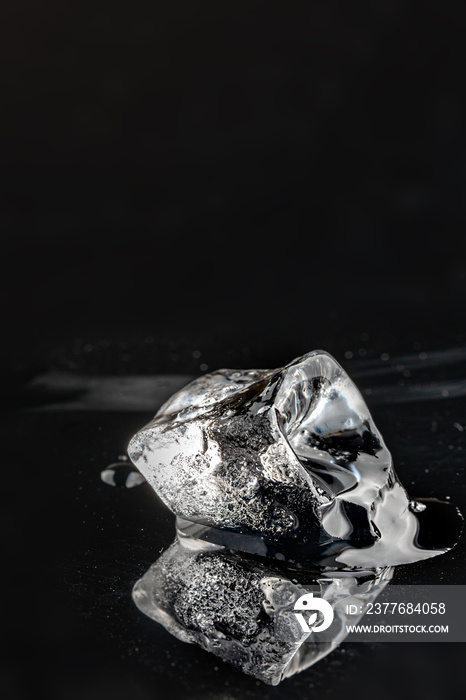 Melting ice cube on black background. Vertical view, close-up