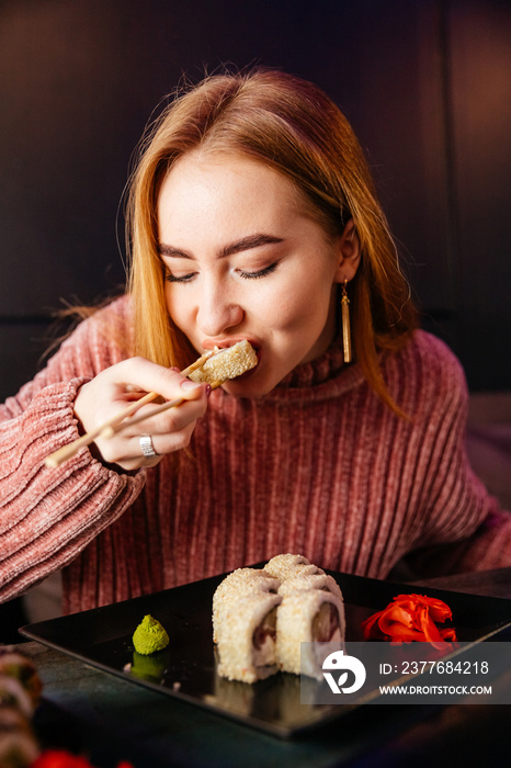 young attractive girl holding a makizushi sushi roll served on black plate on sushibar background