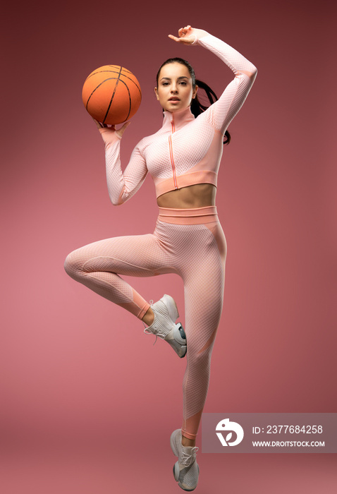 Beautiful young woman with basketball ball jumping in the air