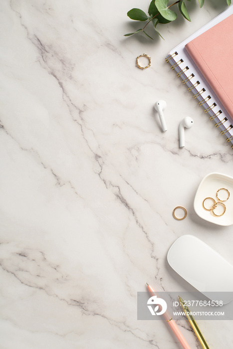 Business concept. Top view vertical photo of workspace pink notepads pens gold rings computer mouse wireless earbuds and eucalyptus on white marble background