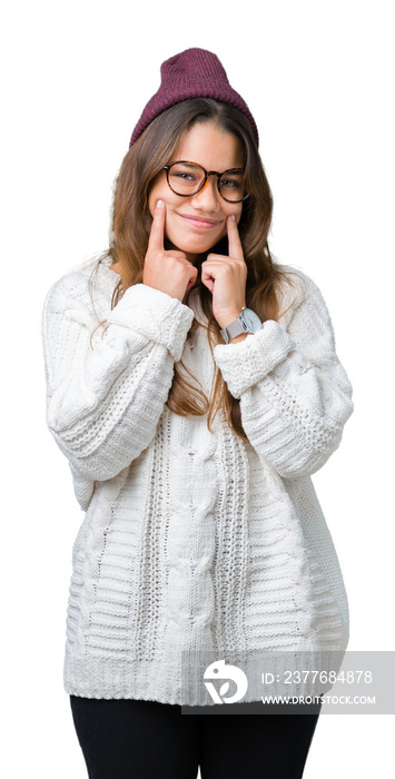 Young beautiful brunette hipster woman wearing glasses and winter hat over isolated background Smiling with open mouth, fingers pointing and forcing cheerful smile