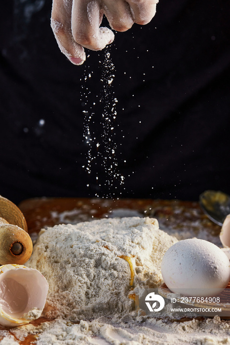 Female hands adding flour to dough, kneading dough for baking. Flour in the air