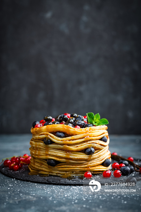 Pancakes with fresh berries and maple syrup on dark background, closeup