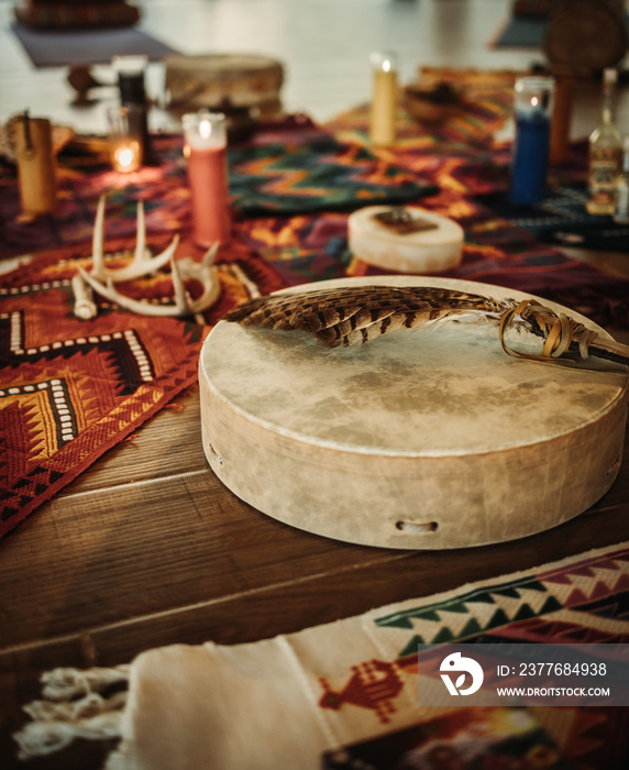 Leather percussion instrument with feather on top and red carpet with indigenous patter in the background with candle during Maya ceremony in Tulum