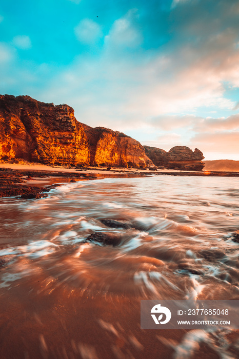 Waves washing over rocks at beach with cliffs in background