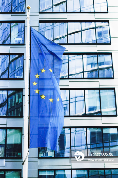 European Union flag waving in front of modern corporate office building, symbol of EU Parliament, Commission and Council.