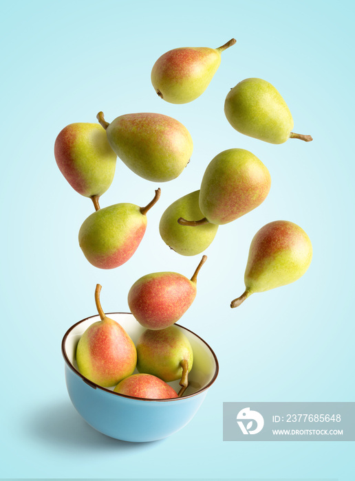 Small pears flying over a bowl, isolated from the blue background, concept of summer and health