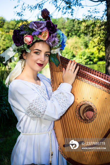 Portrait of a young Ukrainian woman in a white dress with a wreath. Ukrainian musician plays the bandura