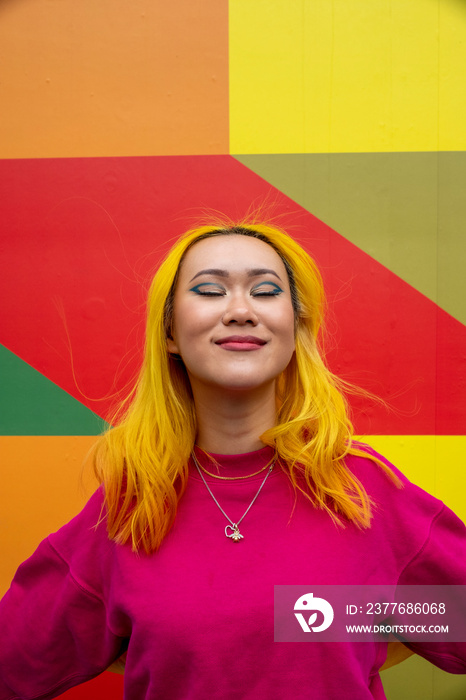 Smiling young woman with yellow hair against colorful wall