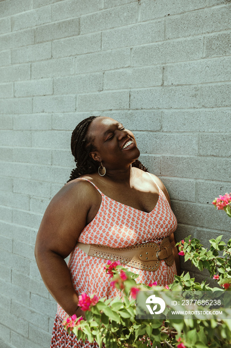 African American woman stands against brick wall and flowers