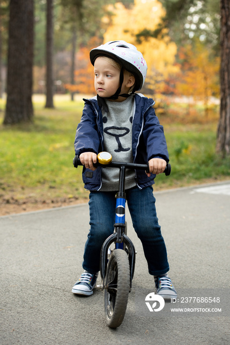 Blond boy in casualwear and safety helmet standing on asphalt road