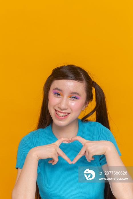 Studio portrait of girl with colorful make-up showing heart shaped gesture