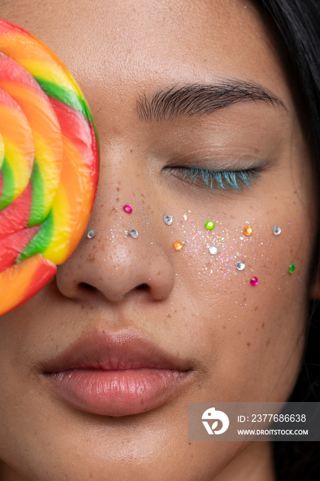 Woman with closed eyes holding colorful lollipop in front of face