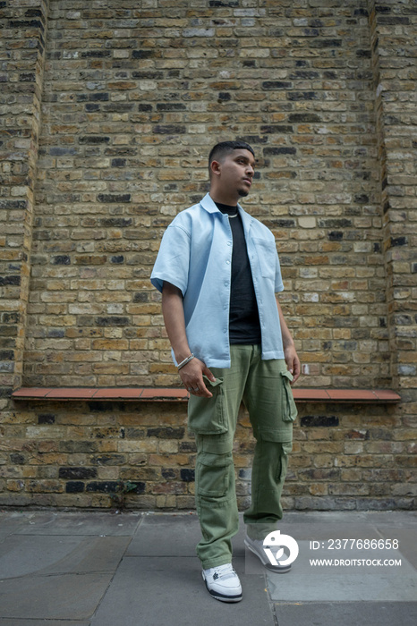 Man wearing unbuttoned shirt and cargo pants standing in front of brick wall