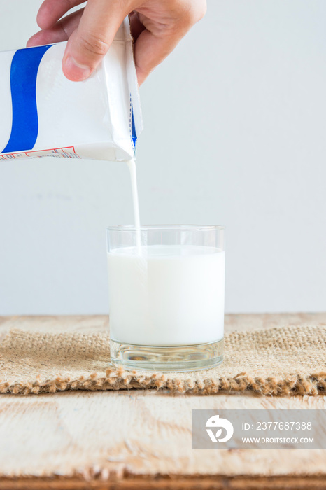 Hand holding a carton of milk poured into a glass on white backg