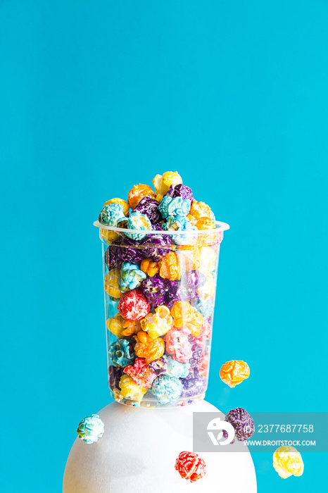 Creative composition with colored popcorn in a transparent glass on a blue background. Modern abstract still life with copy space