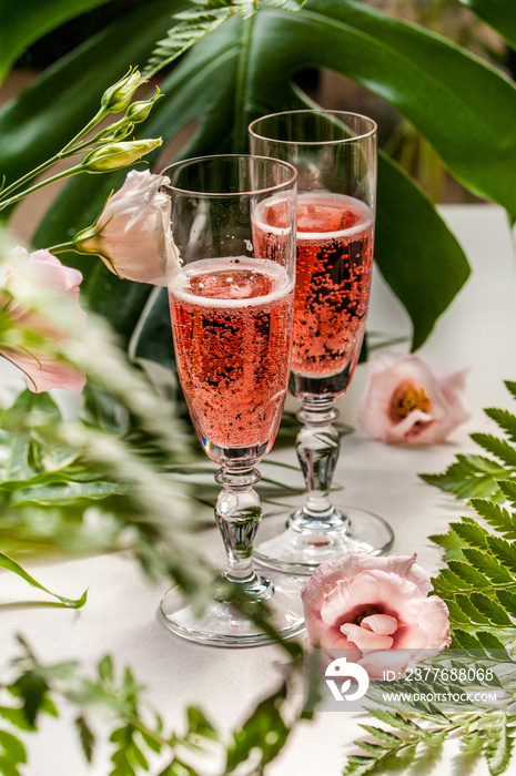 Two crystal glasses of pink champagne with roses and green junge plants