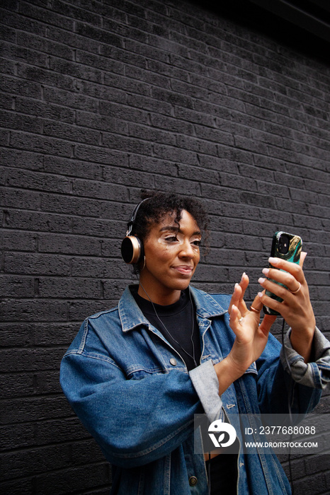 Curvy mixed-race woman with vitiligo taking a selfie in front of a black wall