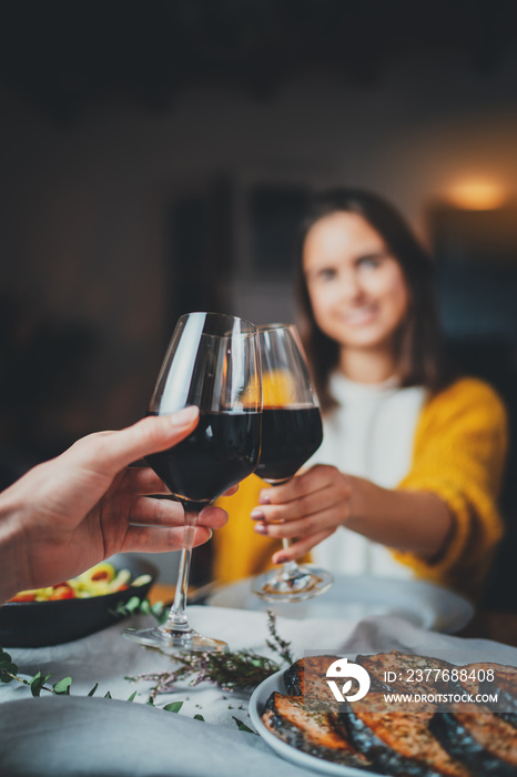 Vertical image of romantic couple making cheers with glasses of red wine, young sweet couple dining at night in cozy restaurant with healthy food, Celebration Cheers Dinner Love Concept