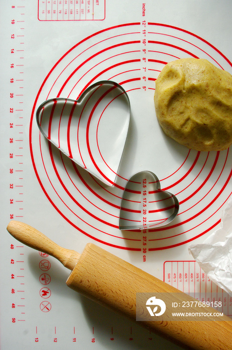 baking scenery with heart shaped cookie cutter, rolling pin for dough, silicone baking mat. Romantic food, photo for recipe book.