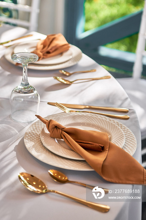 Table setting with sparkling wineglasses, plate with brown napkin and cutlery on table, copy space. Place set at wedding reception. Table served for wedding banquet in restaurant