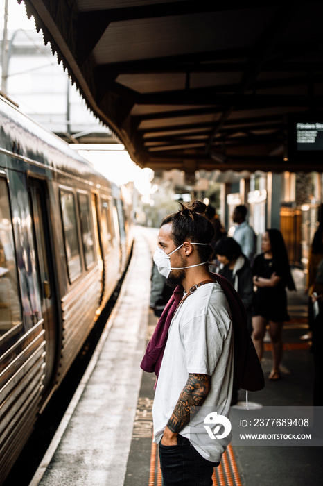 A young caucasian male waiting for the train and wearing a mask