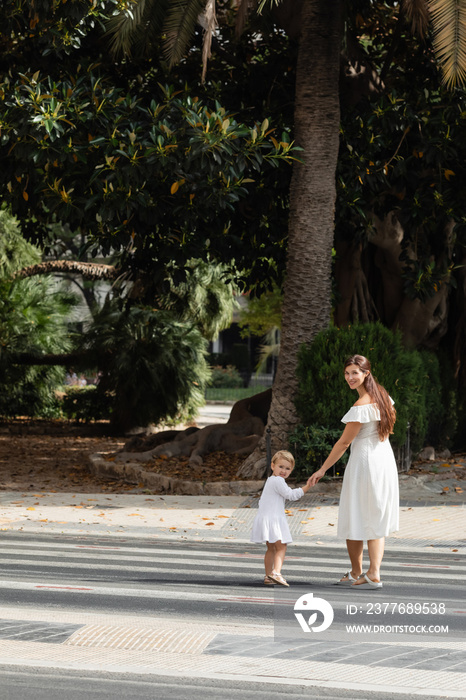 Smiling woman and toddler girl looking at camera on crosswalk in Valencia.