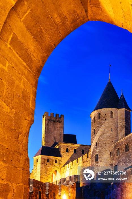 view of the castle through an arch at night in the medieval walled city of Carcassonne (La Cité) in France.