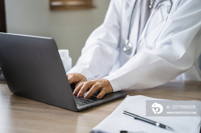 Doctor working with laptop computer and writing on paperwork. in the room.