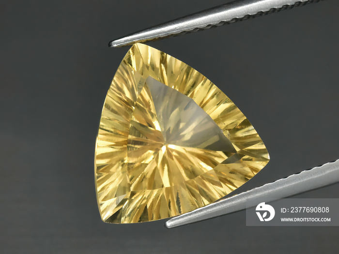 Natural gemstone yellow citrine in tongs on a gray background