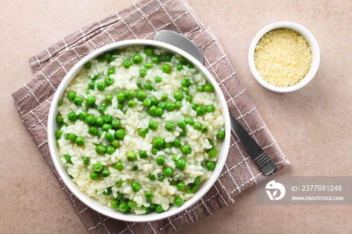 Fresh homemade creamy green pea risotto in bowl, spoon and grated cheese on the side, photographed overhead