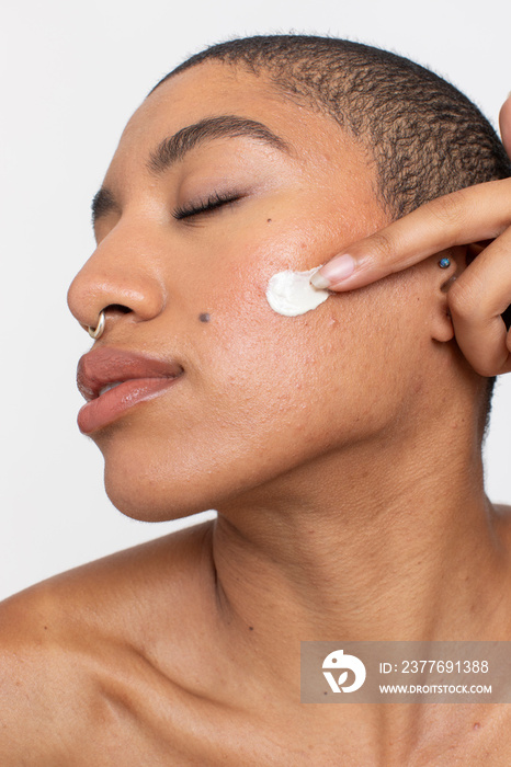 Studio portrait of woman applying face cream on cheek with eyes closed