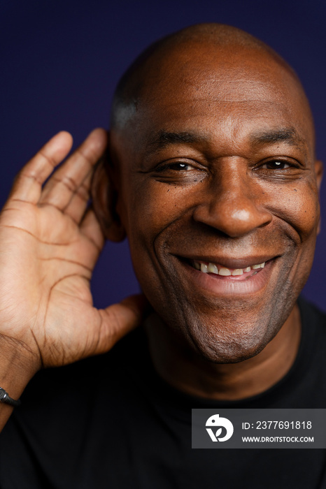 Portrait of smiling man with hand on ear against purple background