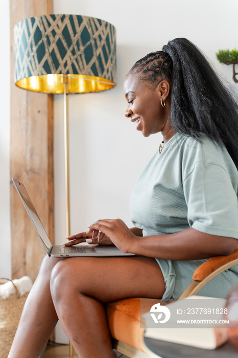 Young woman using laptop while sitting in armchair at home