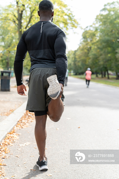 Rear view of athletic man stretching leg in park