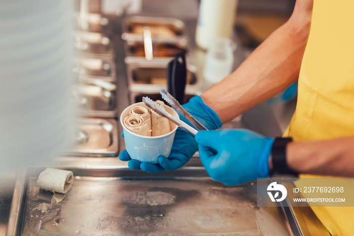 Making of rolled ice cream on a still chilled pan. Handmade frozen dessert, ice cream kiosk.