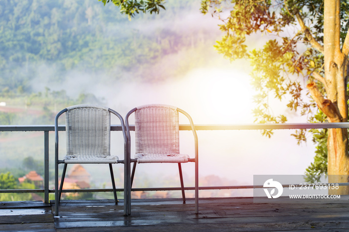 Two chairs placed side by side on the balcony. Behind the valley fog and cool.