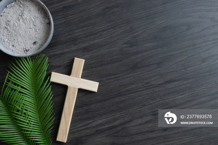 Lent border of palm leaves, cross and bowl of ashes on dark wood with copy space