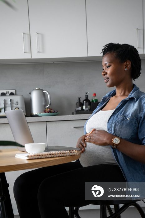 Pregnant woman using laptop in kitchen