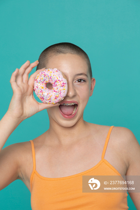 Studio portrait of smiling girl holding donut in front of face