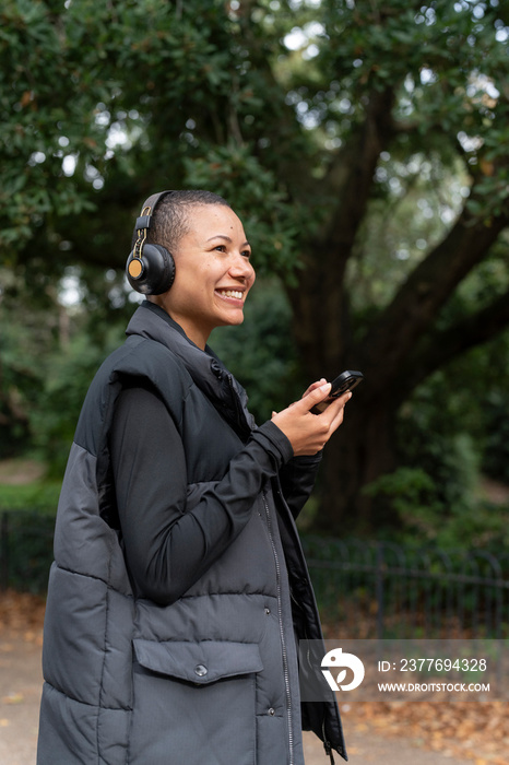 Smiling woman with headphones and smart phone in park