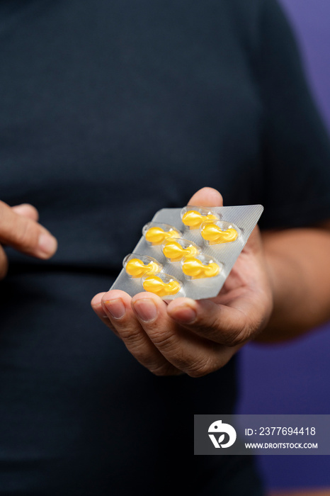 Man holding blister with yellow capsules against purple background