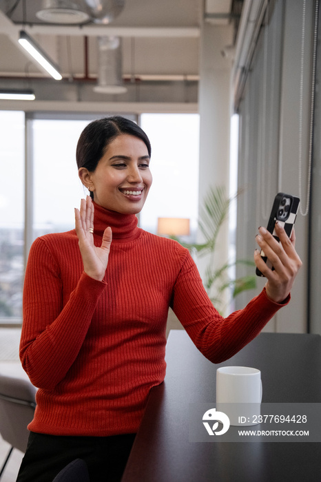 Woman waving to smart phone in office