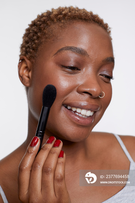 Studio portrait of smiling woman applying blush